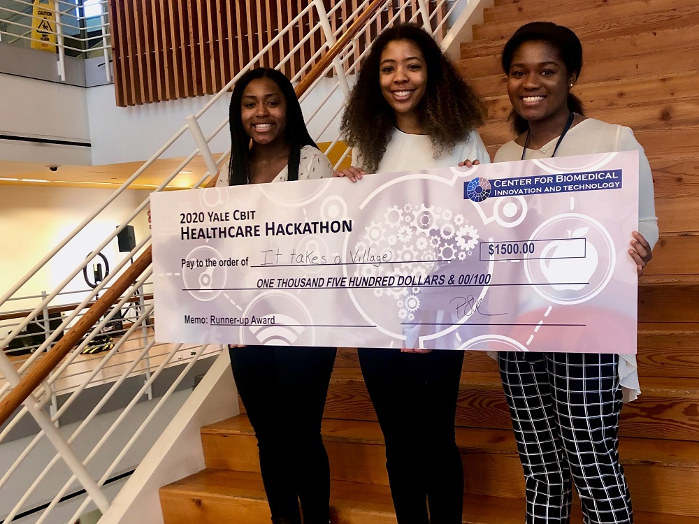 Three female college students hold an award for their app at a hackathon