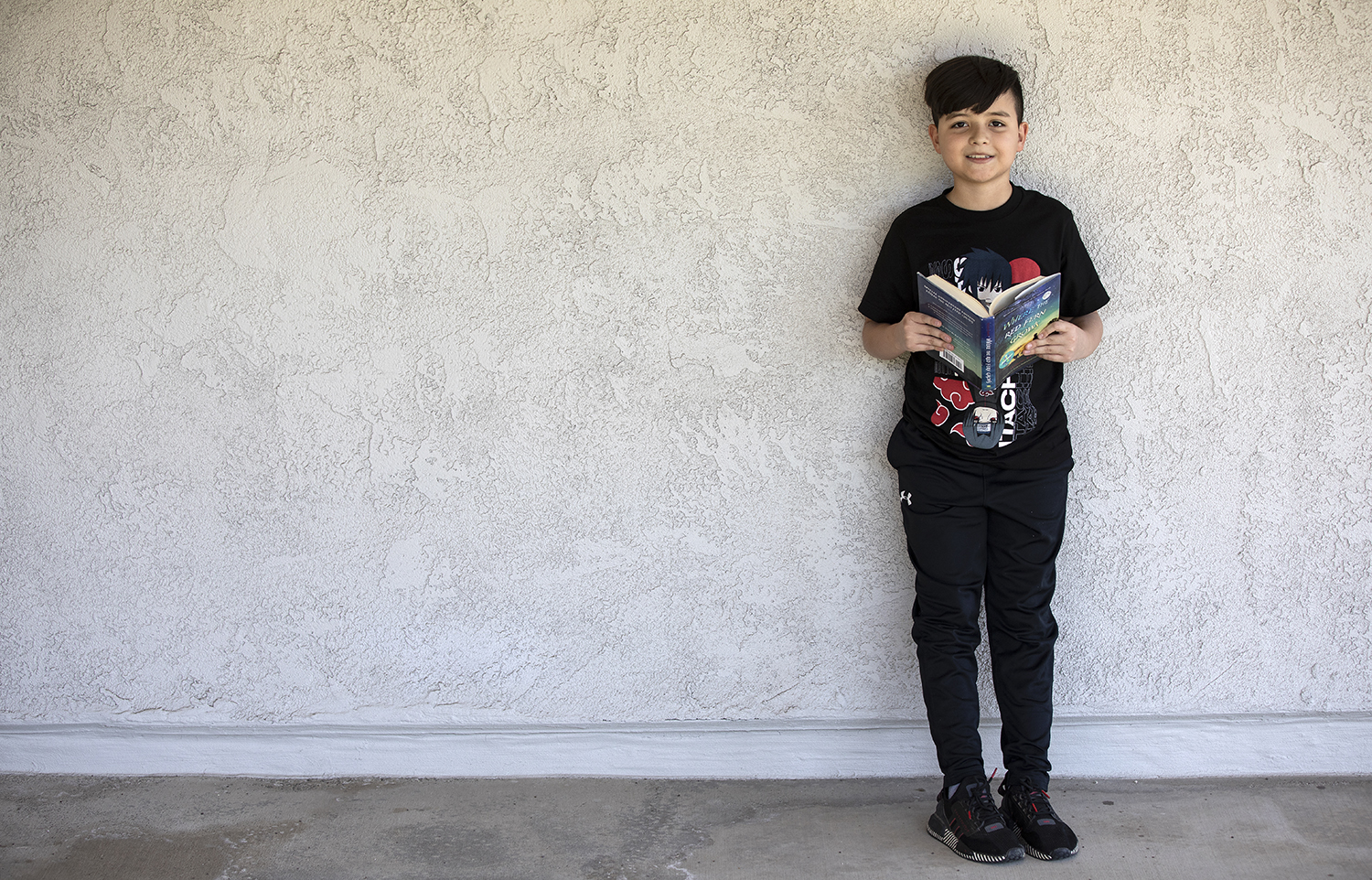 boy stands leaning against a wall, holding a book