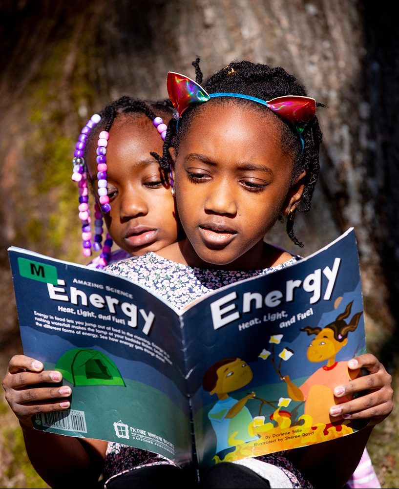 two girls sit close together looking at a book