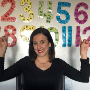 a woman smiles while sitting in a chair in front of a white board with colorful numbers