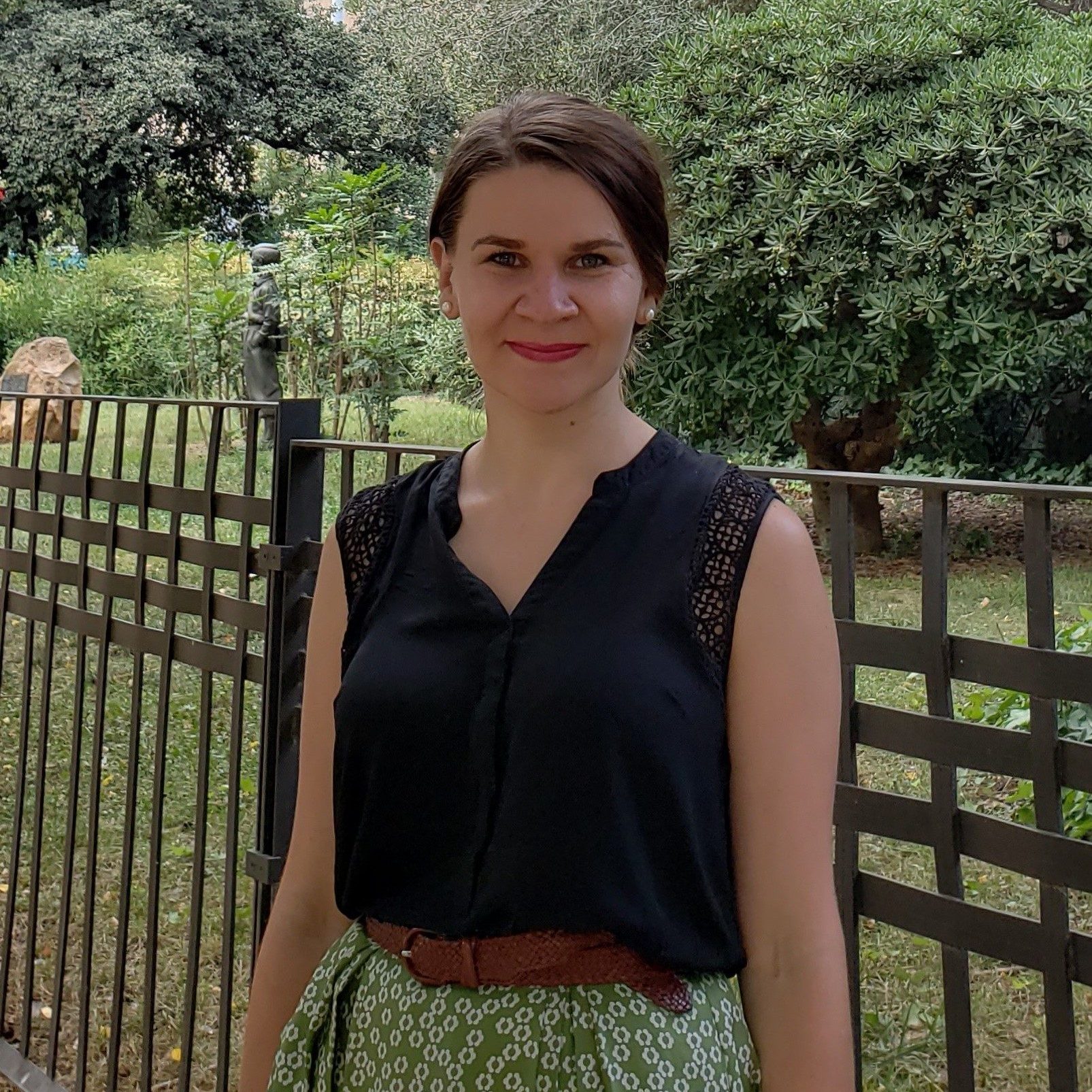 a woman smiles while standing near a fenced garden