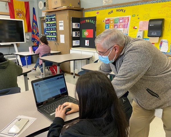 a man leans over a student who is typing on a laptop on a desk