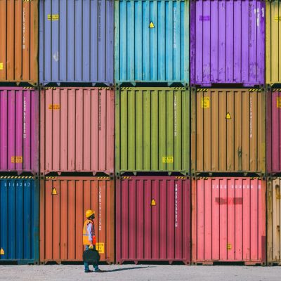 Man wearing a hardhat walking past stacks of shipping containers