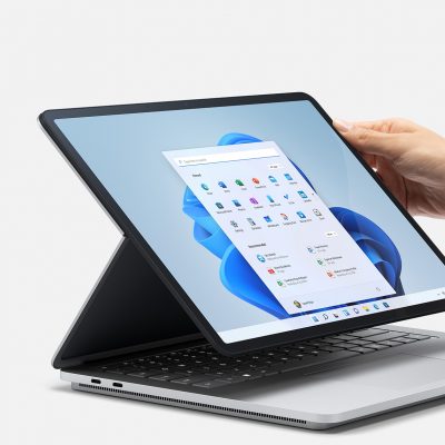 A hand touching a Surface laptop next to a Surface pen