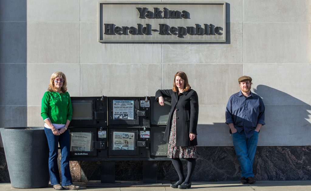Three people stand in front of a Yakima Herald-Republic building
