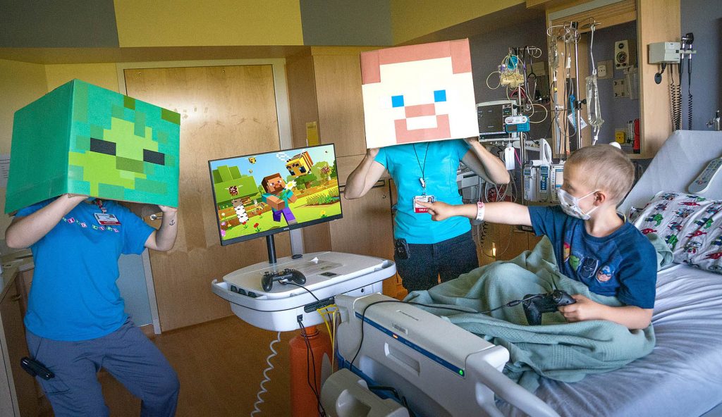 A boy in the hospital plays a video game with two people dressed as Minecraft characters 