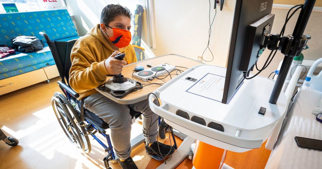 A boy in a wheelchair plays a video game in the hospital