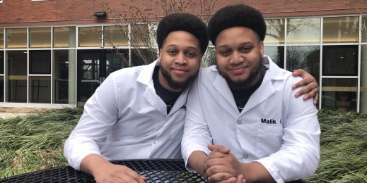 Twin brothers in lab coats sitting next to each other outside
