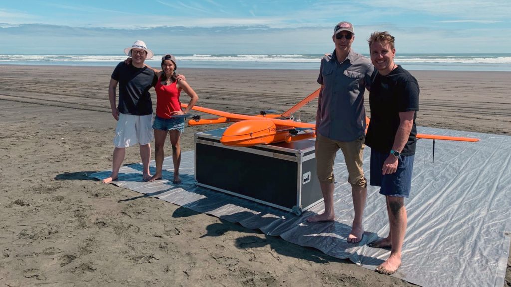 MAUI63 team of three men and a woman pose with the drone on a beach