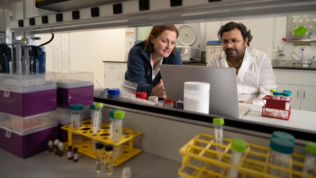 Two people look at a laptop while in a lab