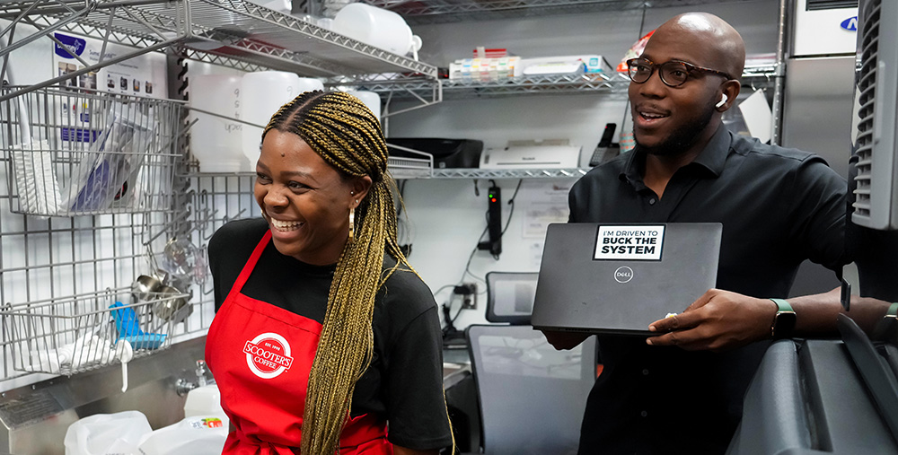 A man and a woman share a laugh in the dishwashing area of a small business