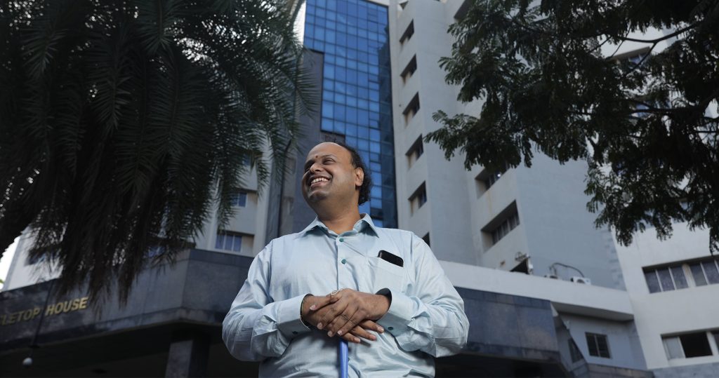 A man who is blind holds his guide cane as he stands in front of an office building