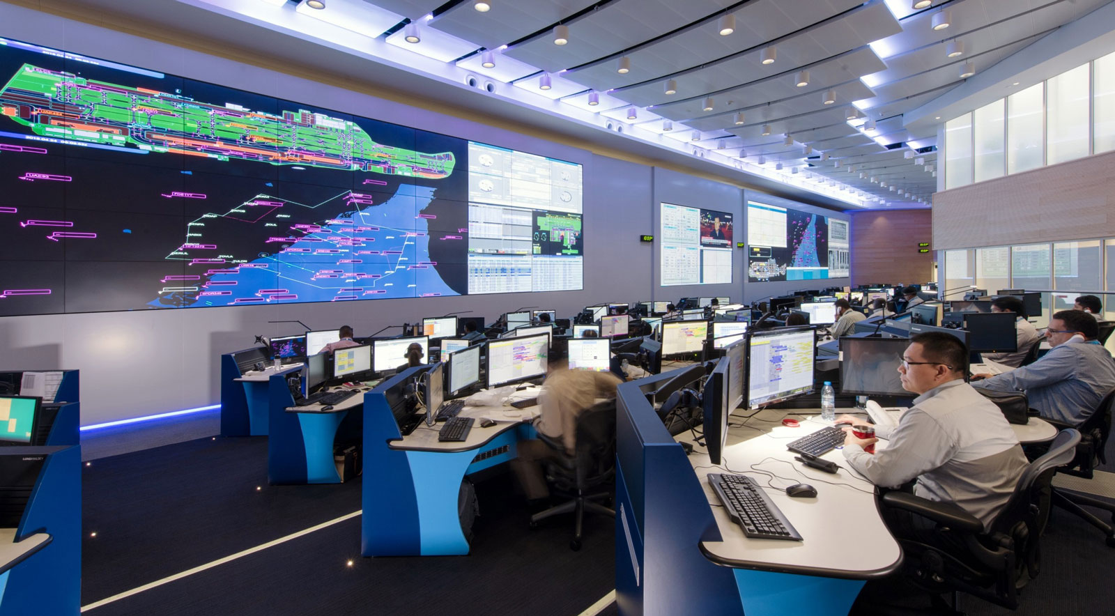 Intelligence room with plenty of computer rows facing a huge digital screen and their attending officers in charge