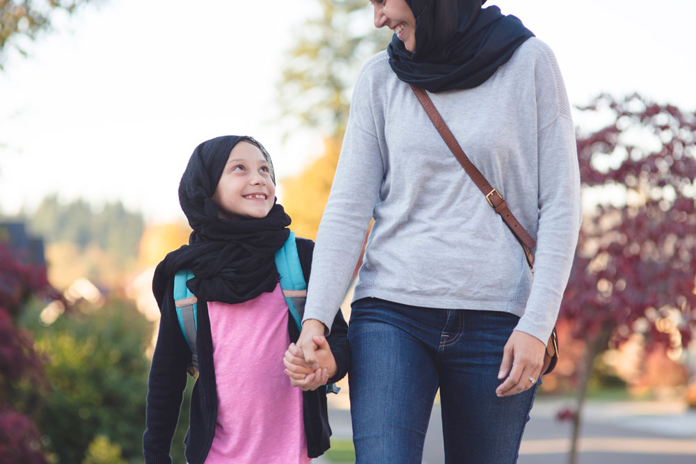 Young girl and a woman walking outside, holding hands, having a conversation and smiling. Education. Hour of Code campaign.