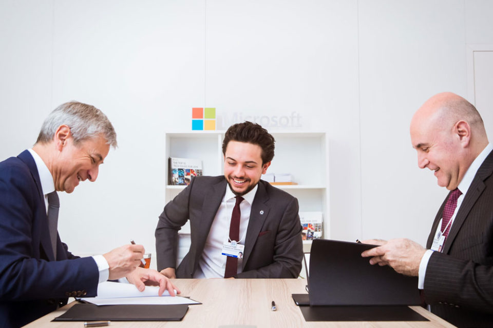 Crown Prince Al Hussein bin Abdullah II setting on a table with two Microsoft representatives gentlemen signing papers