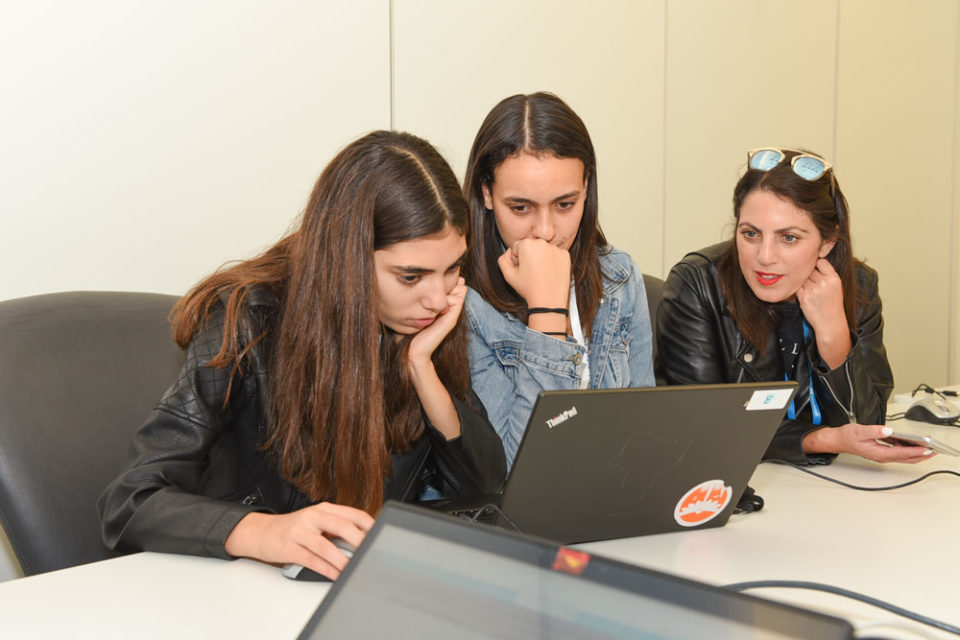 Three young women sitting at a desk looking at laptop