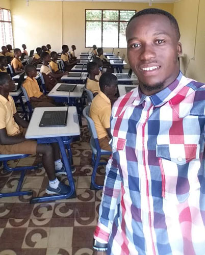 Teacher standing learners sitting at desks behind him