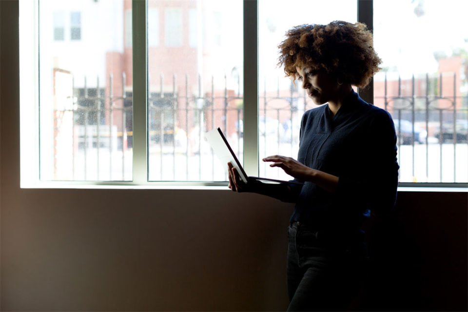 Girl standing next to window looking at laptop
