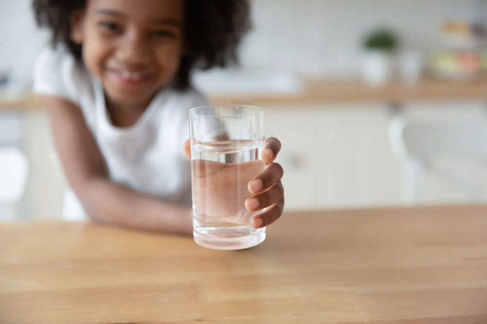 A little girl holding a refreshing glass of water in hand.