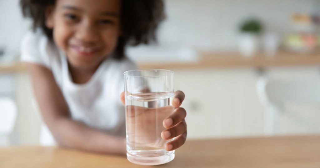 A little girl holding a refreshing glass of water in hand.