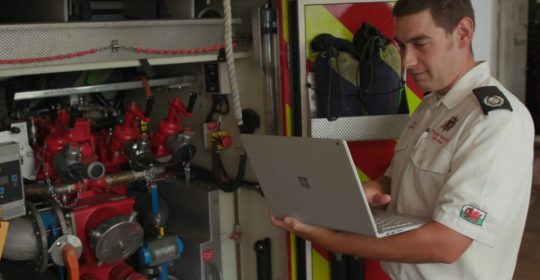 man next to ambulance motor while holding a microsoft laptop