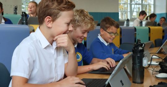 young kids looking at laptops while smiling