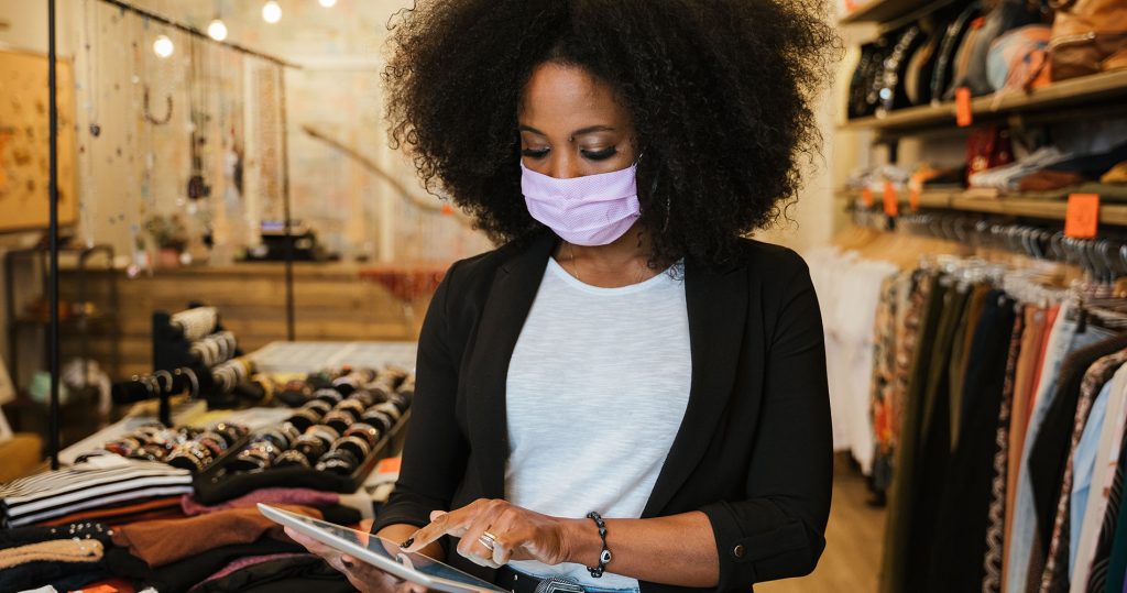 A female shop assistant wearing a face mask checks her tablet in a clothing store