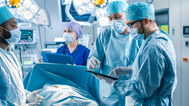 A group of medical professionals consult data from a tablet during surgery.