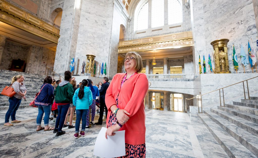Woman with huge smile on her face standing in the crowds in the rotunda of the Washington state Capitol building.