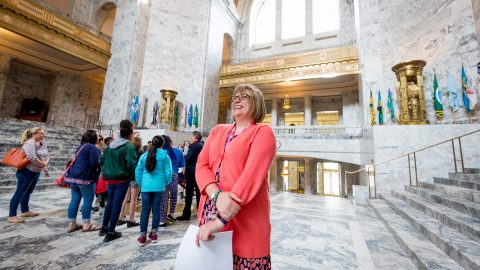 Woman with huge smile on her face standing in the crowds in the rotunda of the Washington state Capitol building.