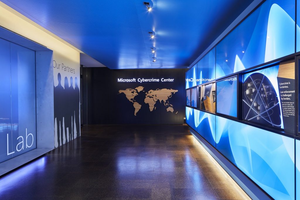 Photo of hallway with brightly lit displays and a sign at end of the hall that says Microsoft Cybercrime Center