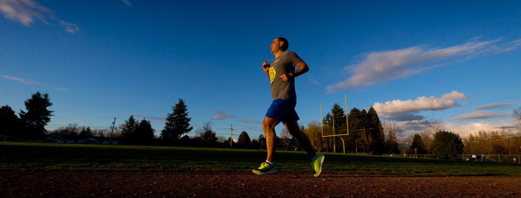 photo of man running under a blue sky and smiling during a track workout