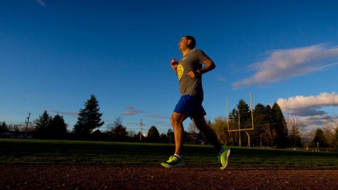 photo of man running under a blue sky and smiling during a track workout