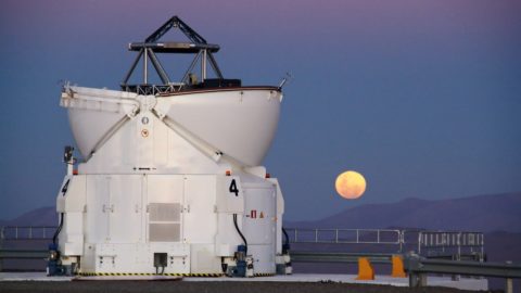 Moon rises at dusk behind a large observatory