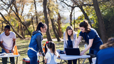 Adults and children using a laptop in a park