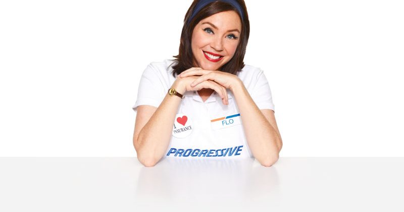 The Flo character from Progressive Insurance ads sits at a table smiling.