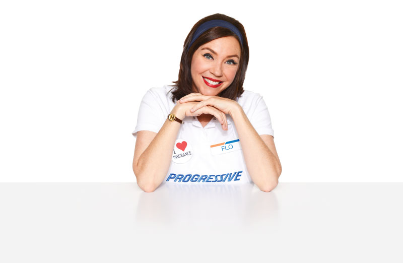 The Flo character from Progressive Insurance ads sits at a table smiling.