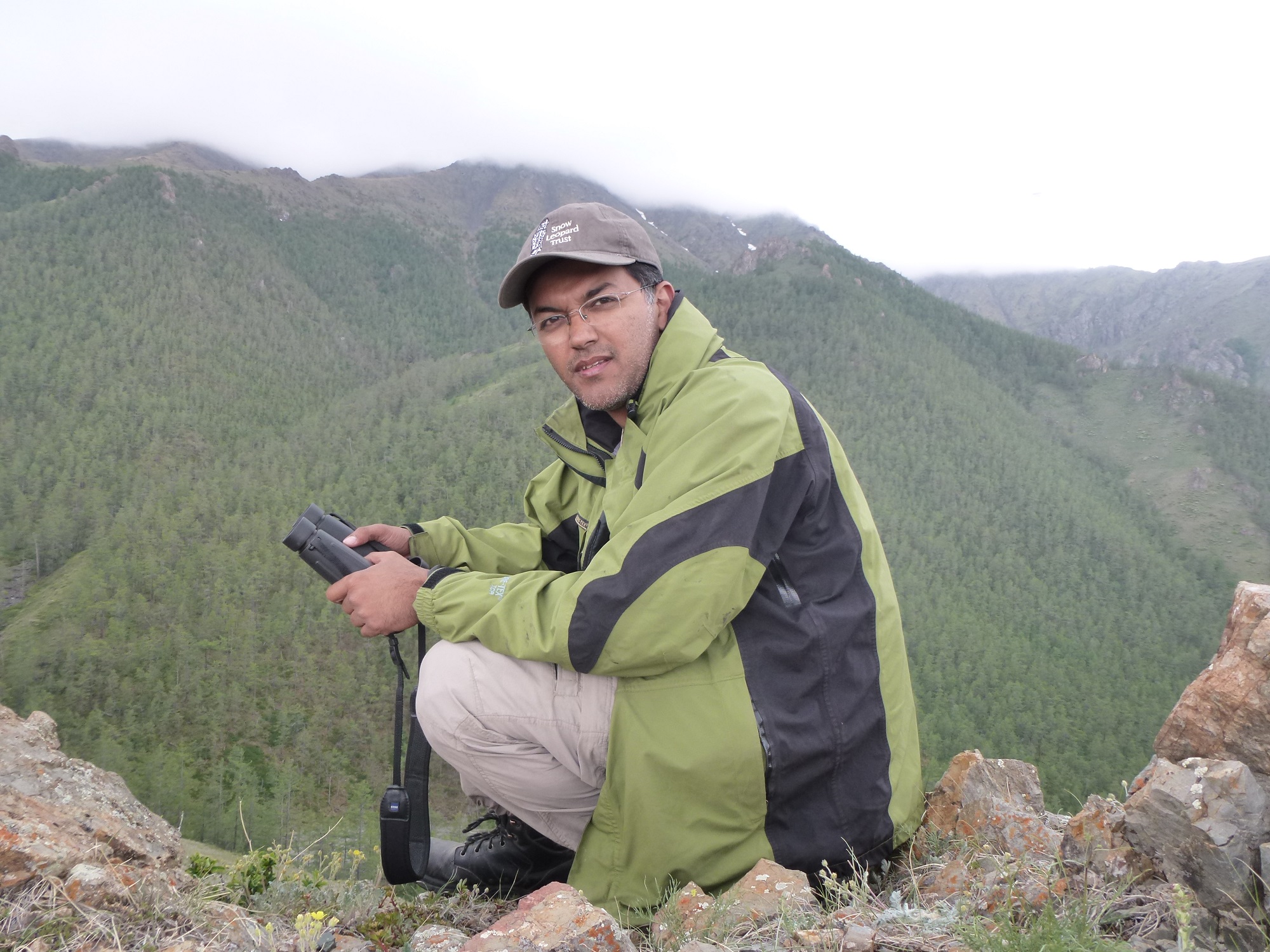 Man sits with binoculars in vast mountain range