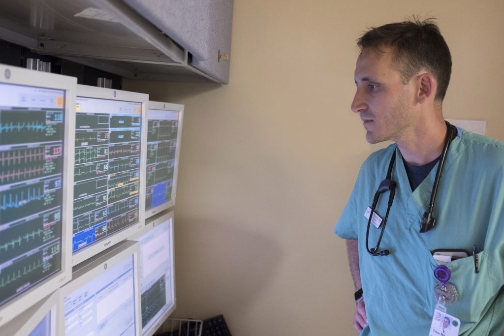 Doctor in scrubs looks at screens of patient data