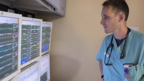 Doctor in scrubs looks at screens of patient data