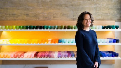 Woman stands in front of display of colorful glass votive holders