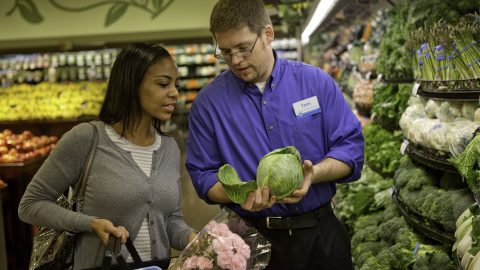 A Kroger customer and associate look at lettucs in the produce section.