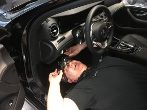 Bauch, wearing HoloLens on his head, lies on his back in a Mercedes-Benz in order to peer under the dashbaord. 