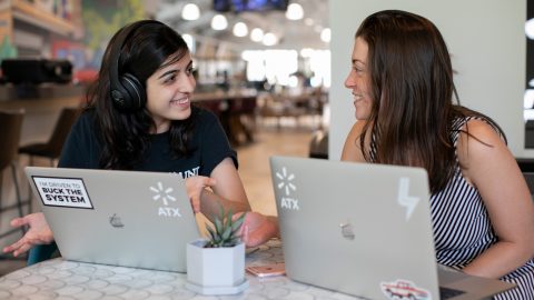 Two women work together behind laptops