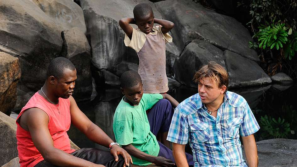 Jochen Moninger speaks with young men outside on a rock outcropping Sierra Leone.