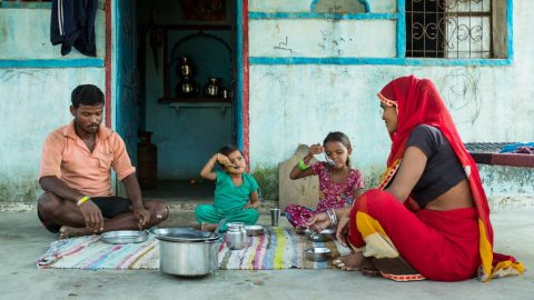 A family eats a meal together sitting on a blanket in rural India.