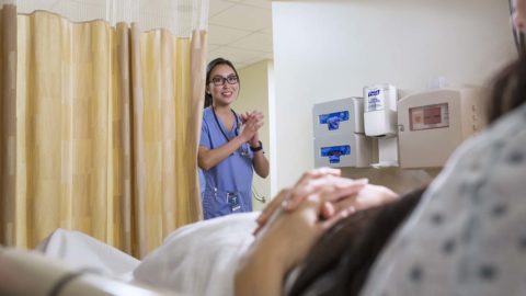Nurse in scrubs rubs hands together near a sanitizer dispenser