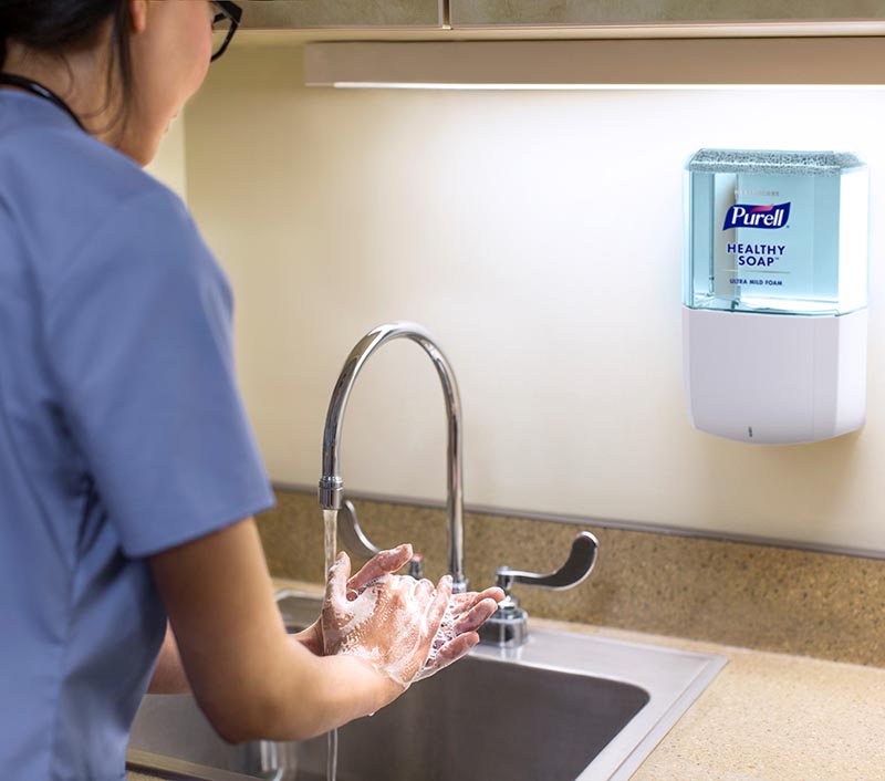 Health care worker in scrubs washes hands at a sink near a soap dispenser