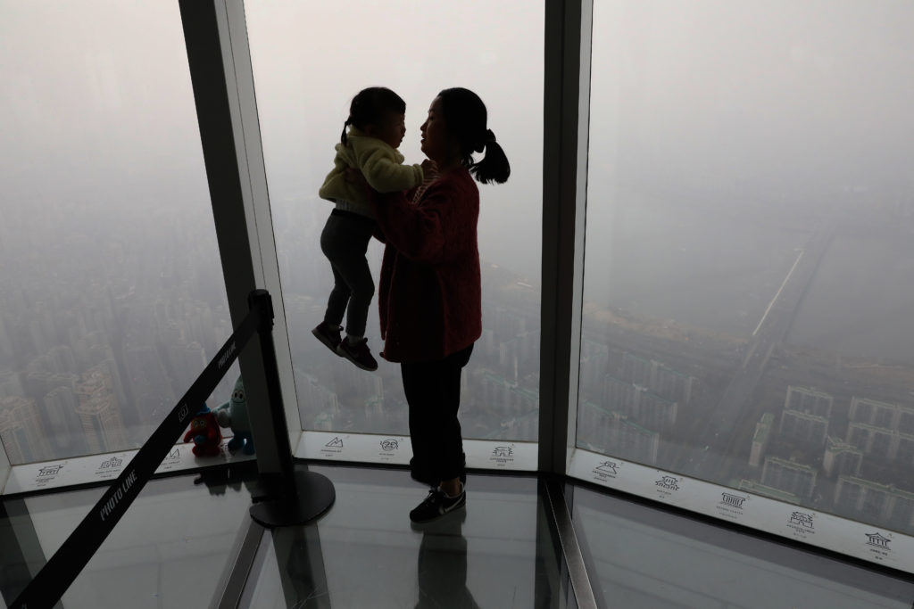 A woman holding her daughter in their home, looking through a window at a view of Seoul on a day with heavy pollution in the air.