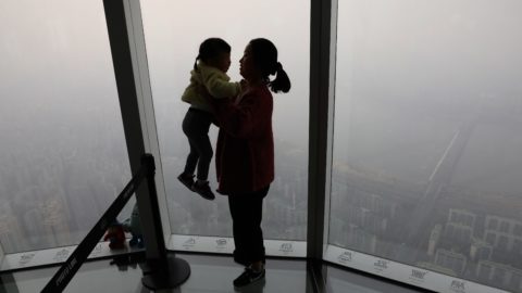 A woman holding her daughter in their home, looking through a window at a view of Seoul on a day with heavy pollution in the air.